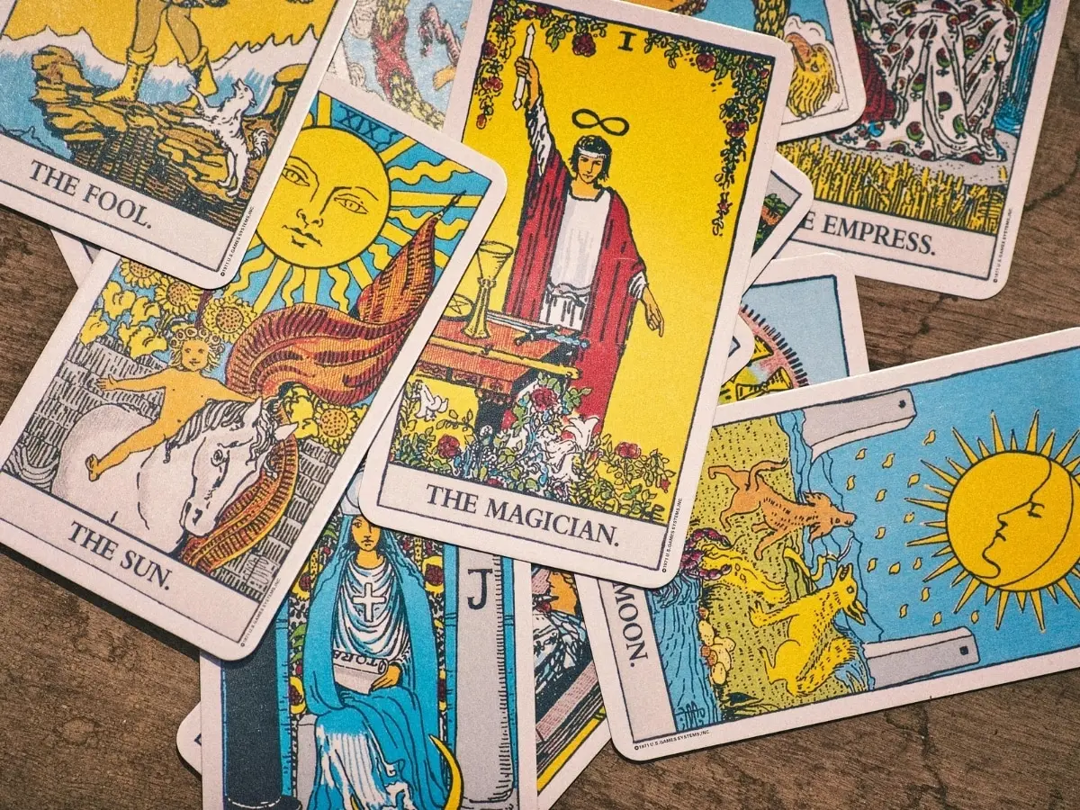 A tarot deck fanned on a dark wooden table, The Sun card on top, with crystals and dried flowers