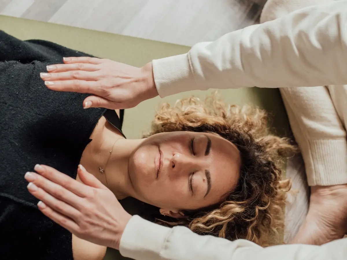 A Reiki practitioner's hands held just above a client who is lying down with her eyes closed